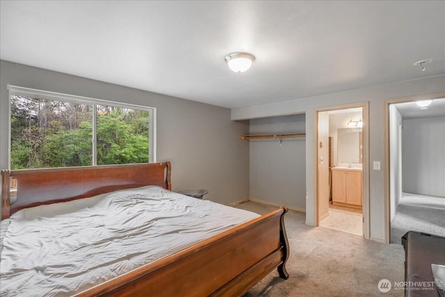 bedroom featuring a closet, baseboards, ensuite bath, a sink, and light colored carpet