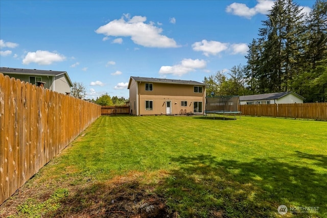 rear view of house with a trampoline, a lawn, and a fenced backyard