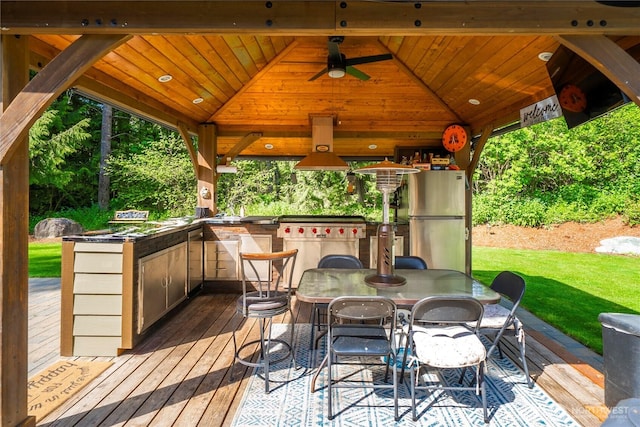 wooden terrace featuring a lawn, a gazebo, an outdoor kitchen, and ceiling fan