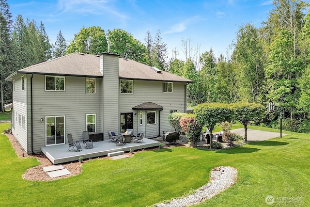 back of property with a lawn, a chimney, a wooden deck, and a shingled roof