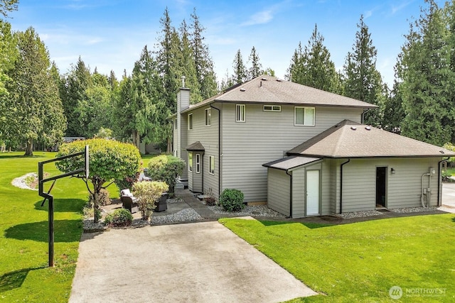 back of property with a lawn, a chimney, a patio, and roof with shingles