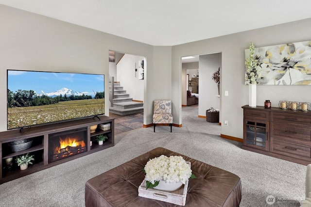 living area featuring carpet flooring, a warm lit fireplace, baseboards, and stairs