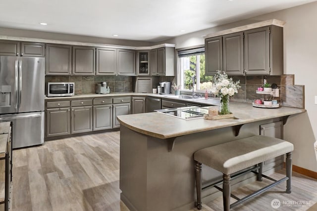 kitchen with light wood-style flooring, a sink, a kitchen breakfast bar, a peninsula, and appliances with stainless steel finishes