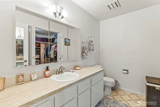 bathroom featuring toilet, vanity, visible vents, a walk in closet, and baseboards