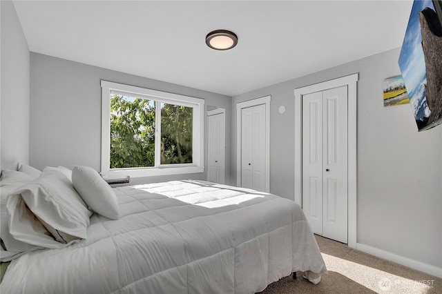 carpeted bedroom featuring baseboards and multiple closets