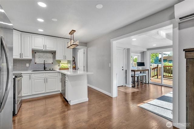 kitchen with a sink, a peninsula, stainless steel appliances, an AC wall unit, and baseboards