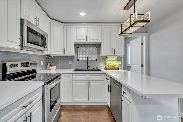 kitchen featuring stainless steel appliances, a sink, white cabinetry, a peninsula, and light countertops