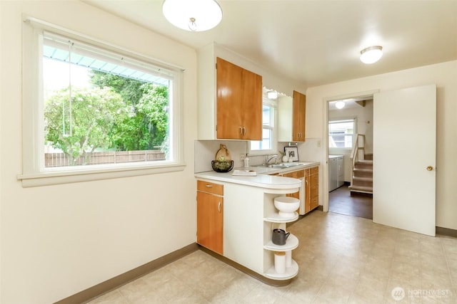 kitchen with washer / clothes dryer, brown cabinetry, a sink, open shelves, and light countertops