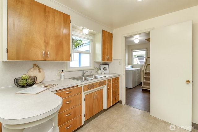 kitchen featuring brown cabinets, light countertops, washer and dryer, and a sink