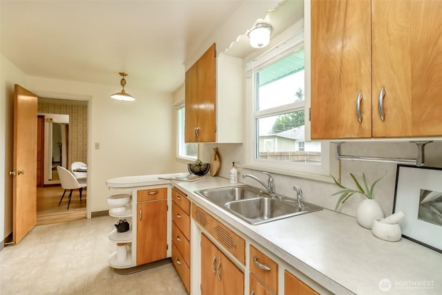 kitchen featuring brown cabinetry, baseboards, a sink, a peninsula, and light countertops