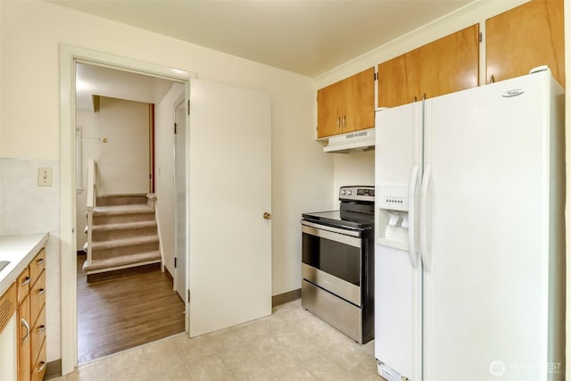 kitchen featuring brown cabinets, under cabinet range hood, light countertops, white refrigerator with ice dispenser, and stainless steel range with electric cooktop