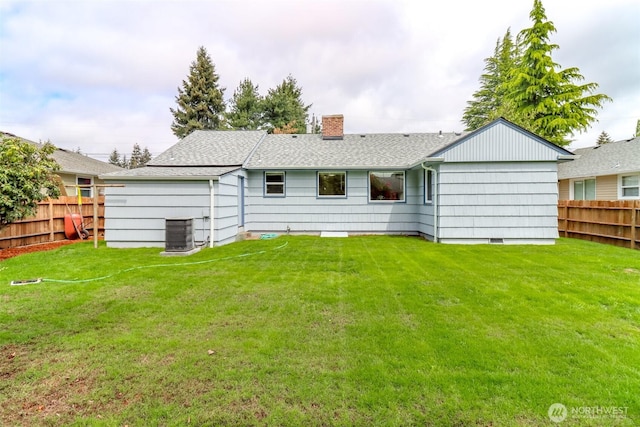 back of property with a chimney, a shingled roof, a fenced backyard, and a lawn