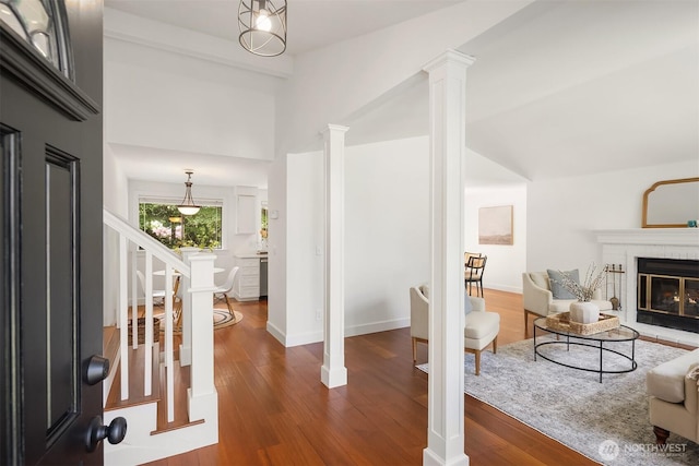 living area with wood finished floors, decorative columns, a fireplace, lofted ceiling, and baseboards