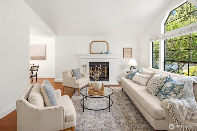 living area featuring a brick fireplace, baseboards, wood finished floors, and high vaulted ceiling