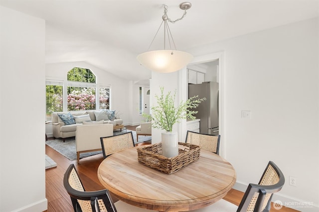 dining room featuring light wood-style floors, vaulted ceiling, and baseboards
