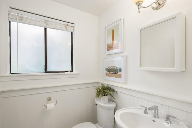 bathroom with a wainscoted wall, toilet, and a sink