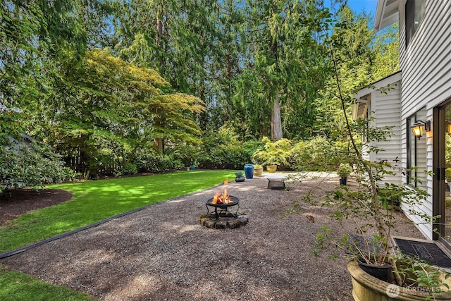 view of grassy yard featuring a fire pit, view of wooded area, and a patio area