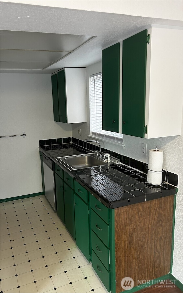 kitchen featuring green cabinets, stainless steel dishwasher, a sink, and light flooring
