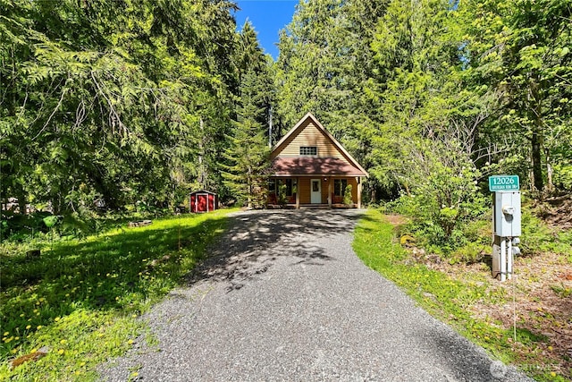 12026 Shuksan Rim Dr, Deming, WA 98244 - view of front of property featuring a storage shed, a porch, an outdoor structure, a wooded view, and asphalt driveway