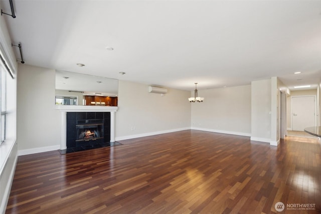 unfurnished living room with wood finished floors, a tile fireplace, a chandelier, an AC wall unit, and baseboards
