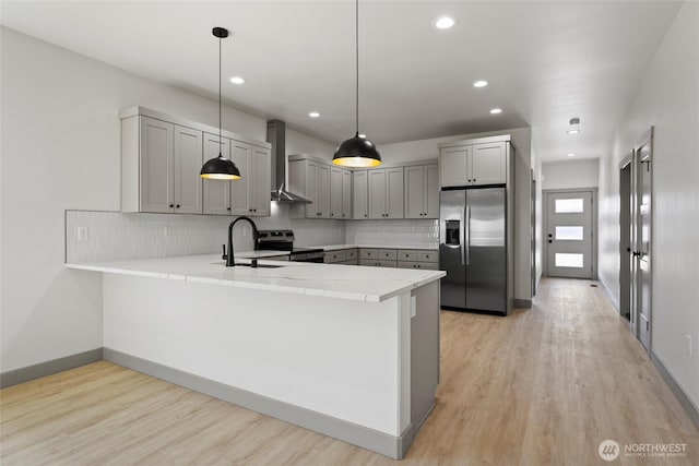 kitchen featuring stainless steel appliances, wall chimney range hood, a peninsula, light countertops, and light wood-style flooring