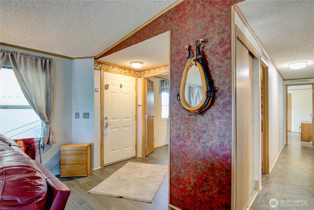 entryway featuring a textured ceiling, crown molding, baseboards, and wood finished floors