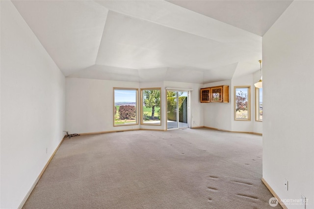 carpeted empty room featuring baseboards and vaulted ceiling