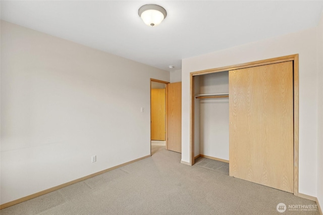 unfurnished bedroom with a closet, light carpet, and baseboards