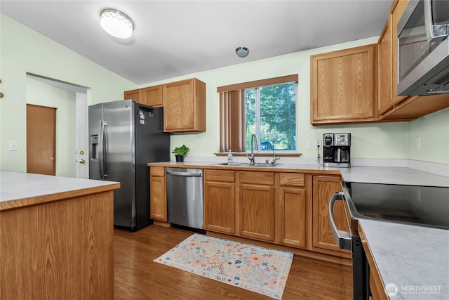 kitchen featuring stainless steel appliances, a sink, vaulted ceiling, dark wood-style floors, and light countertops