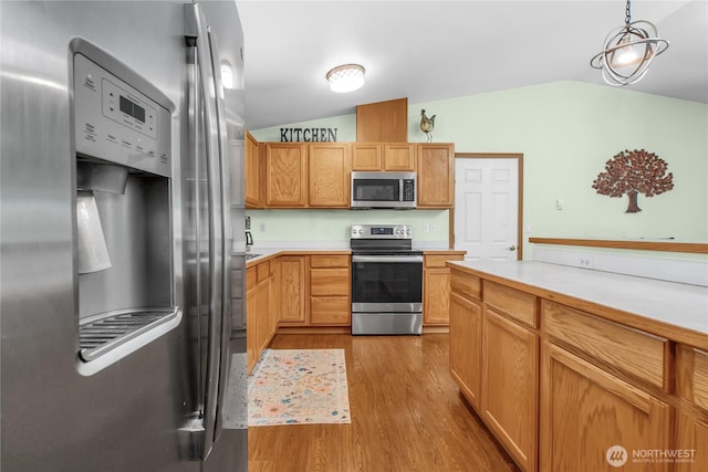 kitchen with stainless steel appliances, vaulted ceiling, wood finished floors, light countertops, and hanging light fixtures