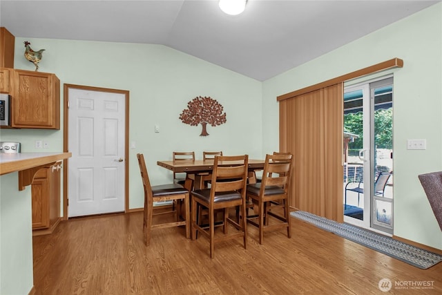 dining room featuring light wood-style flooring, vaulted ceiling, and baseboards