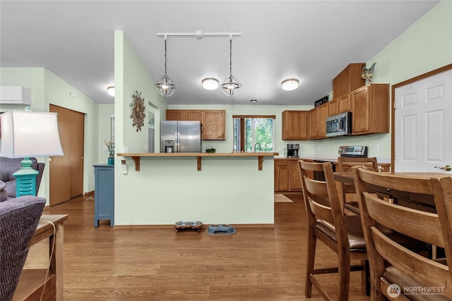 kitchen with appliances with stainless steel finishes, a breakfast bar area, wood finished floors, brown cabinets, and lofted ceiling