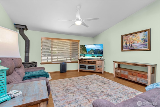living area with a wood stove, ceiling fan, vaulted ceiling, wood finished floors, and baseboards