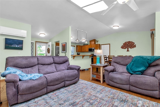 living area with a wall mounted air conditioner, light wood-style flooring, a ceiling fan, lofted ceiling, and a skylight