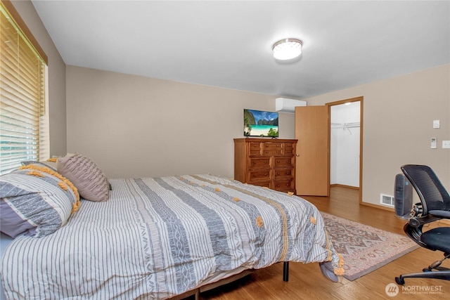 bedroom featuring wood finished floors, an AC wall unit, a spacious closet, and a closet