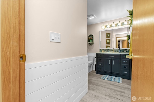 bathroom with toilet, a wainscoted wall, wood finished floors, and vanity