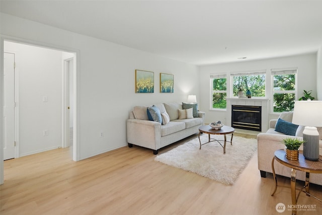 living area featuring light wood-style flooring, baseboards, and a glass covered fireplace