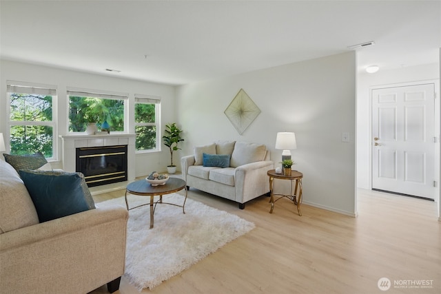 living area featuring visible vents, light wood-style flooring, baseboards, and a glass covered fireplace