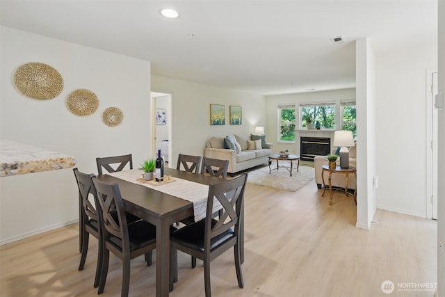 dining area with baseboards, light wood finished floors, a glass covered fireplace, and recessed lighting