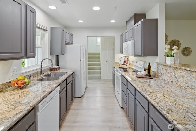 kitchen featuring recessed lighting, white appliances, light stone counters, a sink, and light wood-style floors