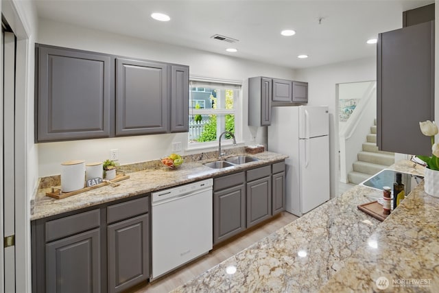kitchen featuring light wood finished floors, a sink, white appliances, gray cabinetry, and light stone counters