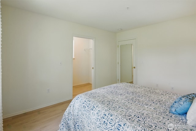 bedroom featuring baseboards, a spacious closet, and light wood finished floors