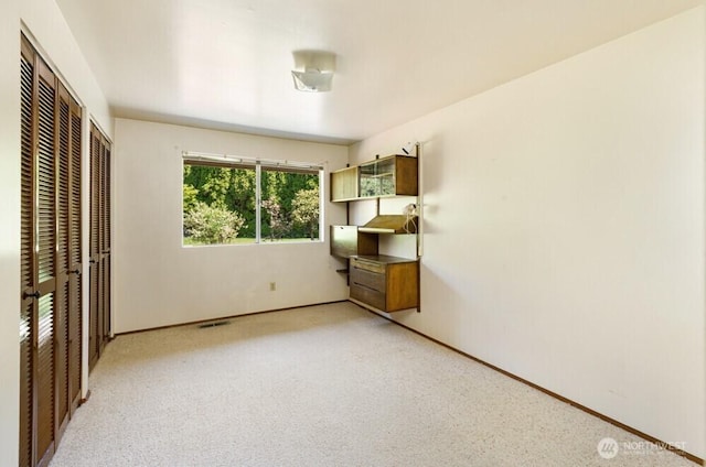 unfurnished bedroom featuring light carpet, baseboards, visible vents, and multiple closets