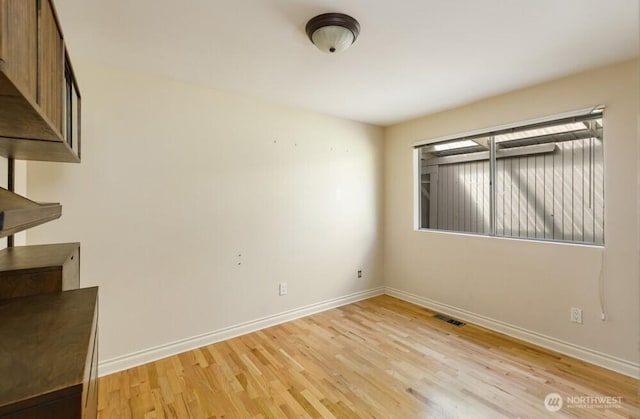 spare room with baseboards, light wood-style floors, and visible vents