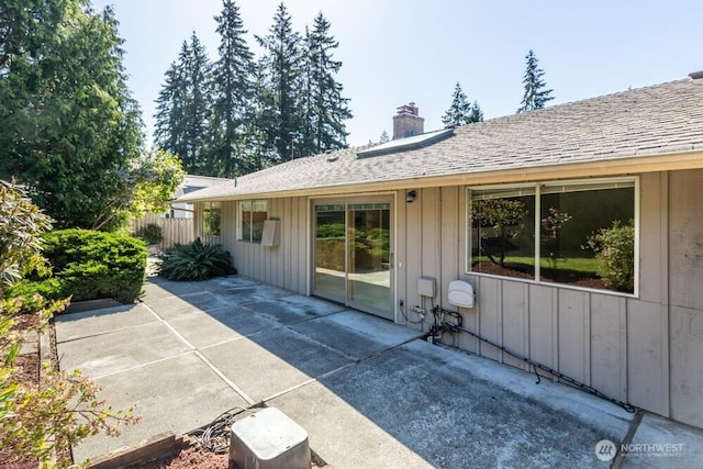 rear view of house with a chimney, board and batten siding, fence, a patio area, and roof with shingles