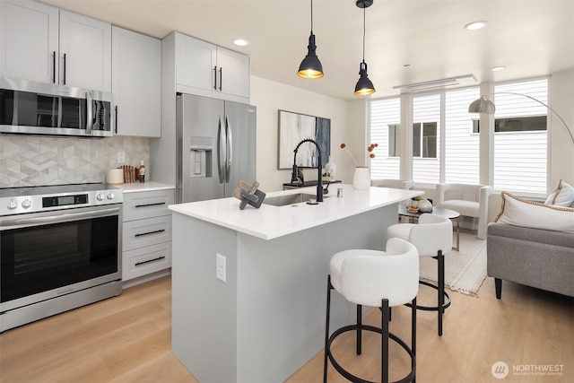 kitchen with stainless steel appliances, a sink, light wood finished floors, open floor plan, and a kitchen bar
