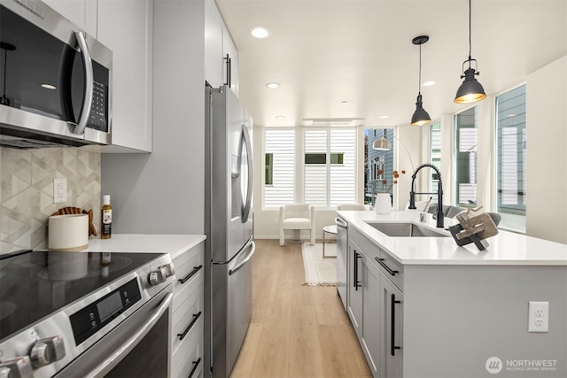 kitchen with stainless steel appliances, a sink, light wood-type flooring, light countertops, and recessed lighting