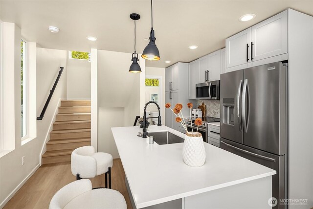 kitchen with stainless steel appliances, a sink, light wood-type flooring, decorative backsplash, and an island with sink