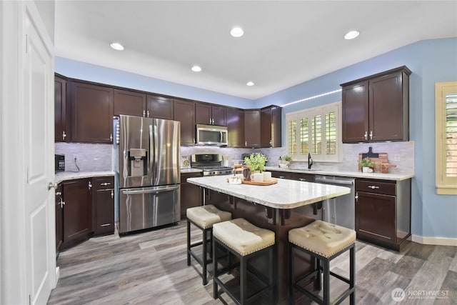 kitchen featuring appliances with stainless steel finishes, a breakfast bar, light wood-style flooring, dark brown cabinetry, and recessed lighting