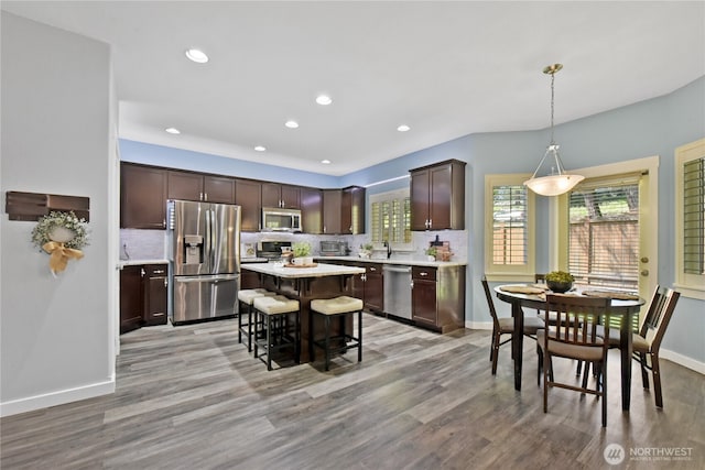 kitchen featuring appliances with stainless steel finishes, a kitchen bar, light countertops, a center island, and backsplash